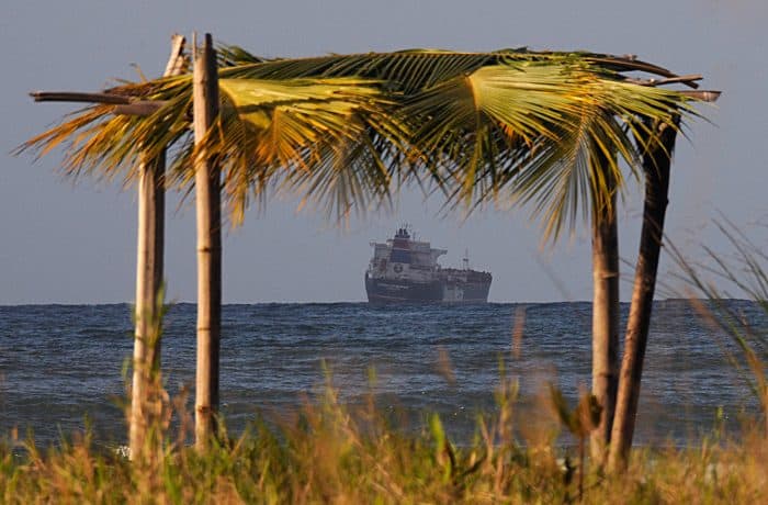 A makeshift beach hut frames a cargo ship waiting to dock at Costa Rica's Moín Port.