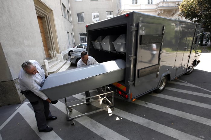 Ten coffins with the bodies of migrants who died in an abandoned lorry are unloaded from a van.