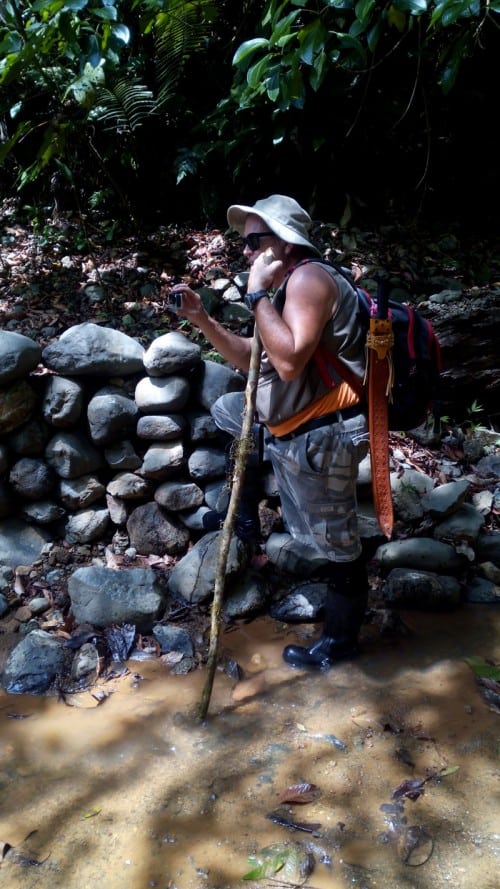 Paul in gold miners' creek, with machete, walking stick and GoPro.