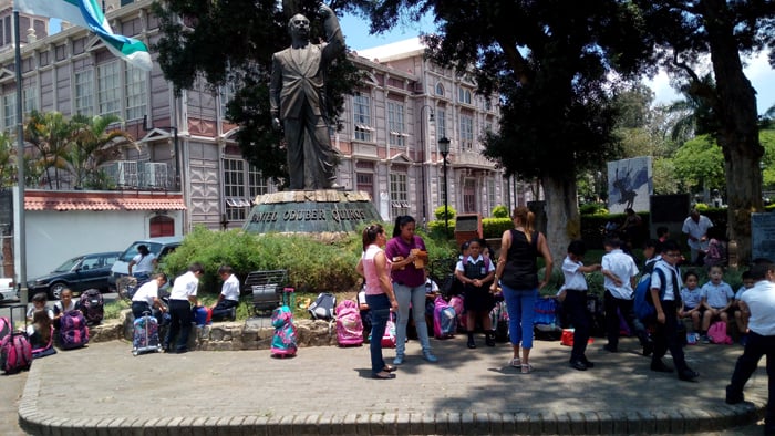 Schoolchildren surround a statue to President Daniel Oduber Quirós, with the Metallic Building in the background.