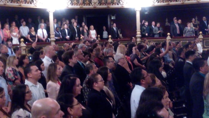 The audience stands to sing the national anthem.