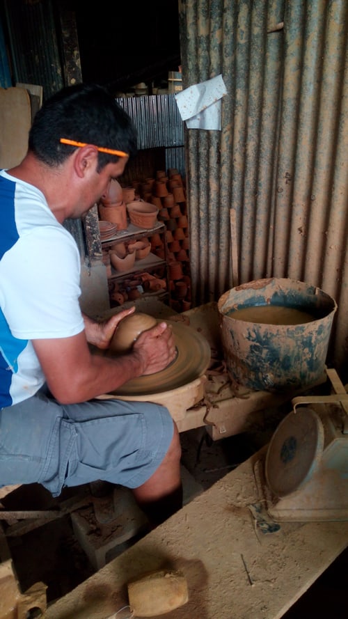 Carlos Marín molds a lump of clay into a rounded pot.